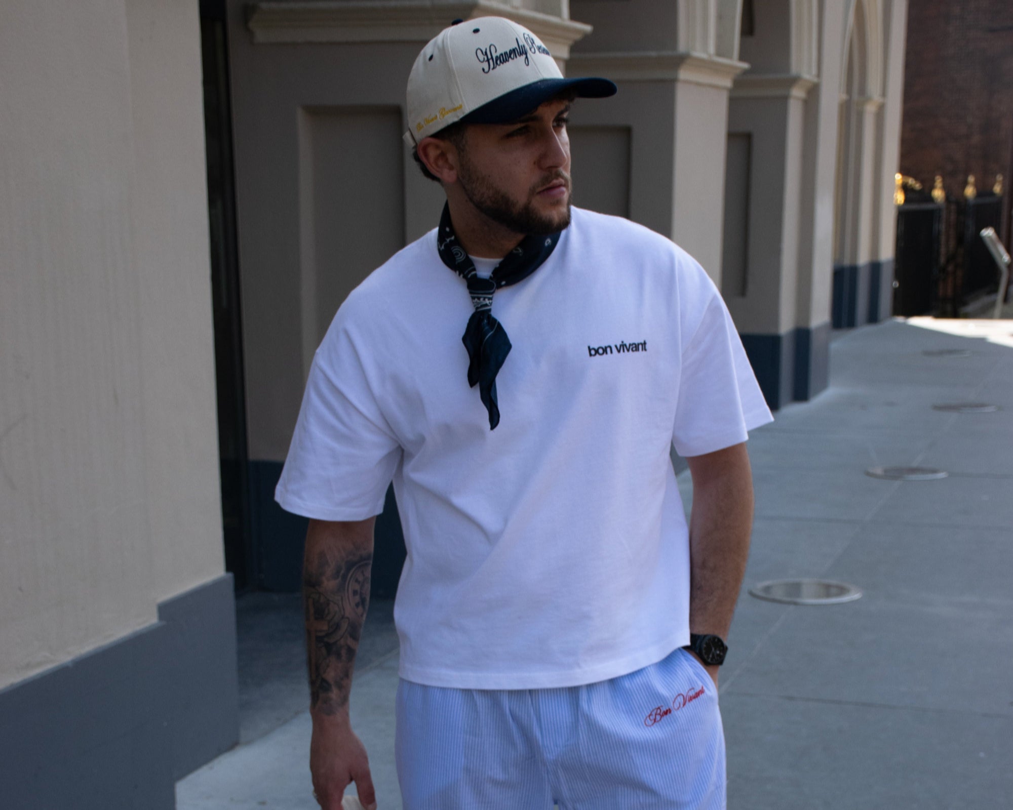 Man in white boxy t-shirt and striped pyjama pants holding a beige tote bag on a sidewalk.