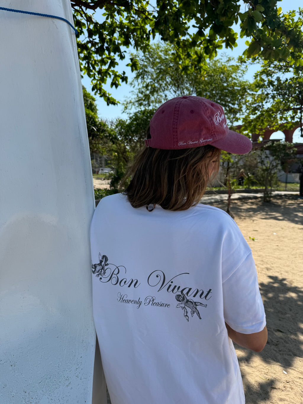 Person wearing a white shirt with text and a pink cap outdoors